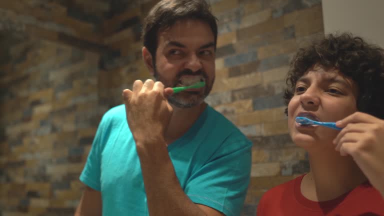 Father and son brushing teeth together at home