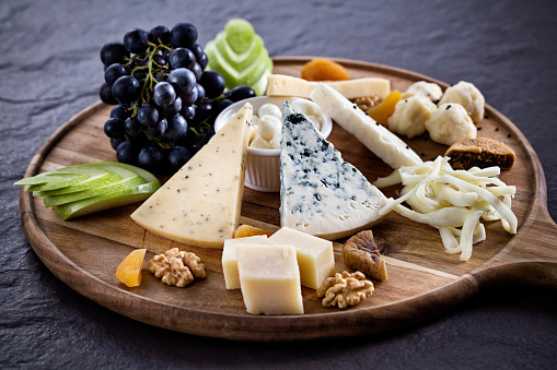 Variety of cheeses and grapes on wooden board.