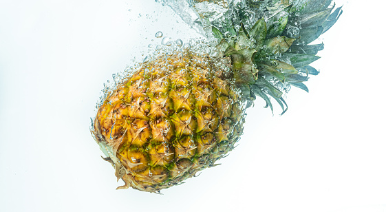pineapple is dropped into clear water isolated on white background. Fruit splash theme.