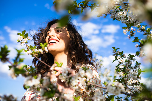 A beautiful young woman is smiling in a blooming orchard on a sunny spring day