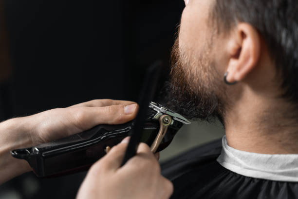 istock Beard shaving in barbershop. Barber with dreadlocks trim handsome bearded man. 1318673886