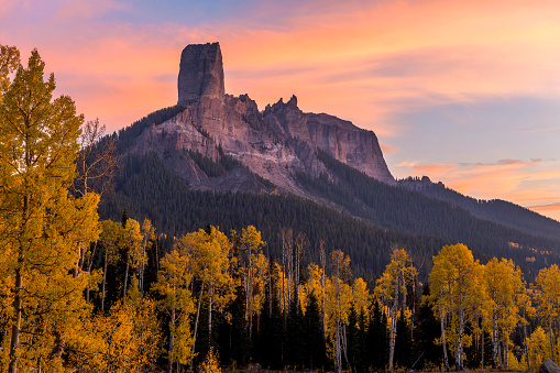 A colorful Autumn sunset view of Chimney Peak rock formations, 11,781 ft (3,591 m), surrounded by golden aspen grove, as seen from Owl Creek Pass, Ridgway, Colorado, USA.