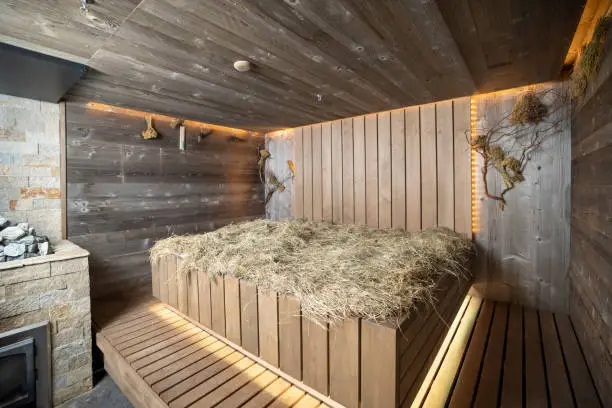Interior of a wooden sauna, steam room, bathhouse with hay on wooden bench. Stylish russian sauna.