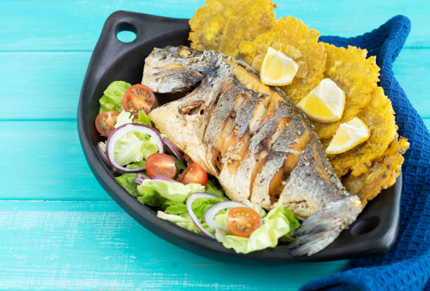 обжаренная рыба с салатом и патаконами на синем фоне. копирование пространства. - grilled bananas стоковые фото и изображения