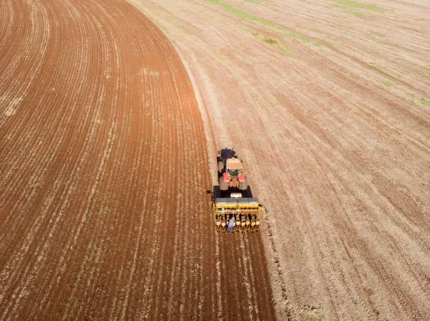 Tractor with seeder in the field. Sowing of corn, Maize in soil, with pneumatic sowing machine during spring season. farmer on tractor with a seeder processes the field..