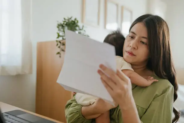 Woman holding paper various expense bills and plans for personal finances at her home.