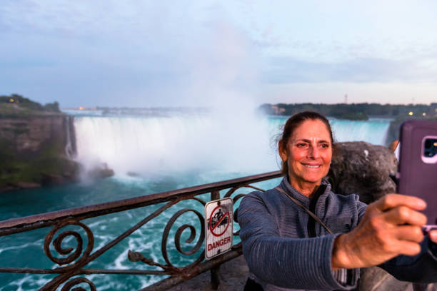 turysta robi selfie przed wodospadem niagara, ze znakiem niebezpieczeństwa na poręczy bezpieczeństwa - niagara falls falling people usa zdjęcia i obrazy z banku zdjęć