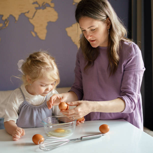 maman apprend au petit enfant à cuisiner tout en passant du temps à la maison - break eggs domestic kitchen breaking photos et images de collection