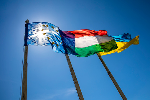 Banderas de Hungría Ucrania y la Unión Europea ondeando en el polo contra el cielo azul photo