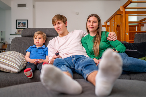 Young cheerful family sitting on a sofa in a living room and watching tv.