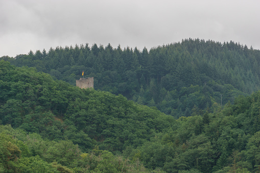 top of tower of an old castle ruin behind a hill surrounded by green forest, Manderscheid, Germany