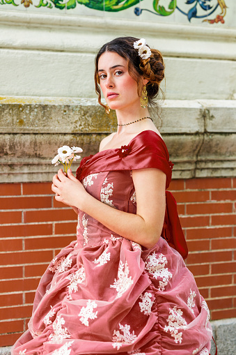 She is a victorian woman 19th century posing in red dress into a park with flowers