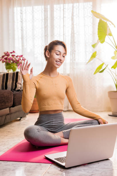 istock Personal trainer entering with laptop computer in a virtual classroom video conference at home during quarantine. Young hispanic woman yoga teacher doing video call for a yoga class 1318713646