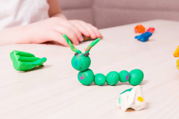 istock a small child sculpts a caterpillar from green plasticine on a wooden table, the development of fine motor skills of hands, playing with a child at home, a caterpillar from plasticine in the foreground 1318715921