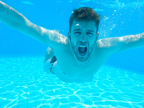 Closeup of man diving in a swimming pool. He's moving towards camera very close to the bottom. Looking at camera.