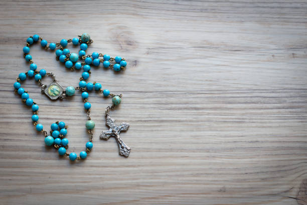 Blue rosary prayer beads with silver crucifix on wood background with copy space