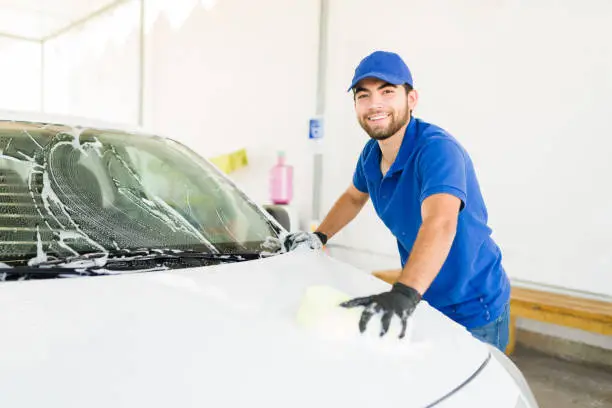 I like my job at the car wash. Attractive young man smiling and making eye contact while washing a car at his job at the auto detail