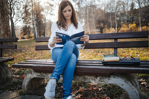 Girl sitting on bench in public park and reading book during free time