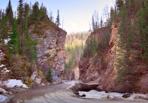 The road between the high rocks along the mountain river Chibitka in the spring. Nature of Siberia, Russia