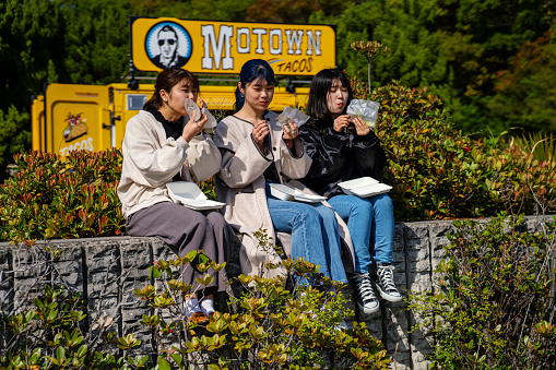 Three young women sitting outside eating take-out lunch from a food truck in Japan