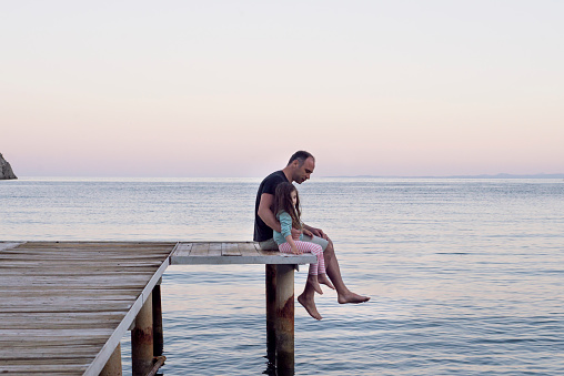 A father and his daughter spending some quality time together while sitting on a sea dock