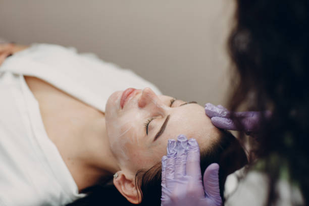 jovem recebe massagem facial com creme de cosméticos em spa de beleza - peeling beauty treatment human face beautician - fotografias e filmes do acervo