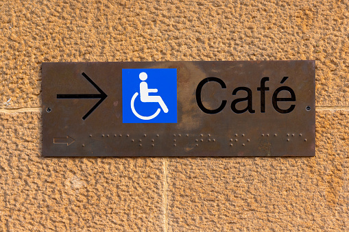 Metal cafe sign with blue wheelchair icon.