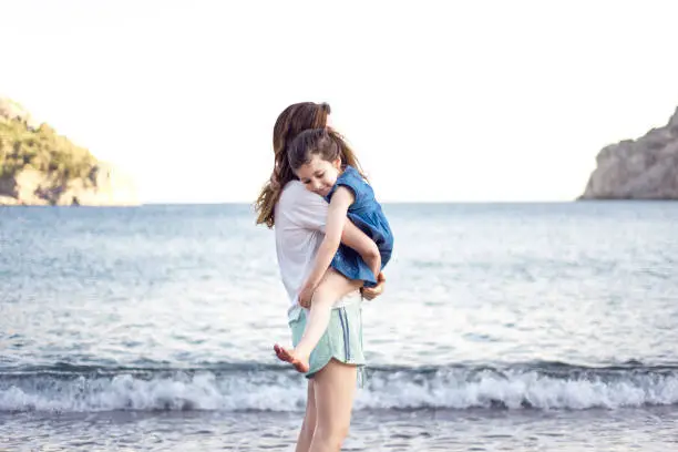 Little girl hugging her mom on the beach, sea in background