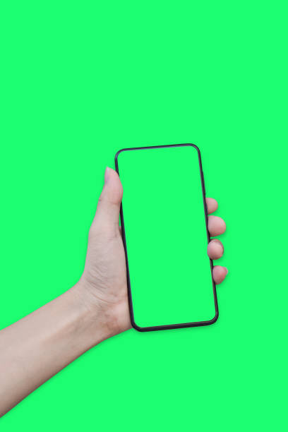 istock Hand holding smartphone with green screen isolated on green background. 1318742839