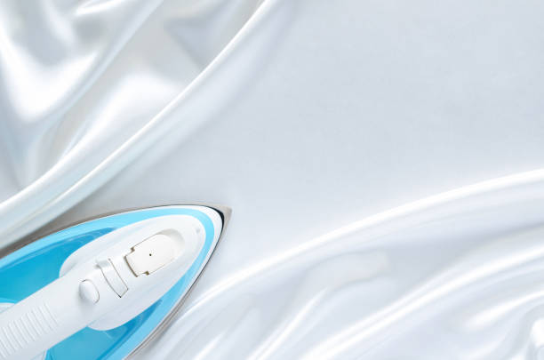 Electric iron on smooth and wavy white cloth texture with space for text. Housekeeping concept.