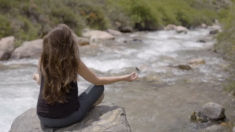 Beautiful free and wild woman sitting in buddha pose on the River in lotus position medicine yoga asana balance kundalini energy every day routine practice good for woman health mindfulness