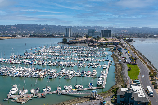An aerial view of the Emeryville Marina on a sunny day. Boats fill the marina and tall buildings in Emeryville in the distance.