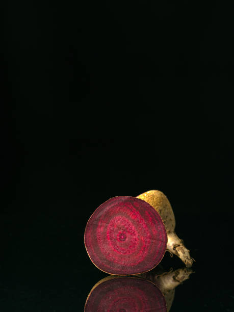 View to the cut raw beetroot. Black background with reflection. Two part of beet. Low key technique. Vertically standing vegetable