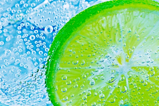 Lemon slice and ice cubes with bubbles in cold carbonated drink.