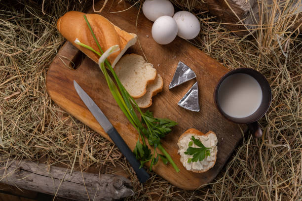 Breakfast with boiled eggs and milk. Sliced bread and milk in a mug. Wooden table and hay.