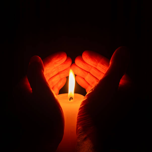 istock Hands holding a burning candle in a heart shape on dark background. Vertical format 1318773731