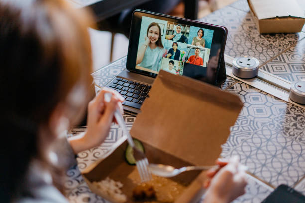 giovane donna videochiachia colleghi durante la pausa pranzo - multi tasking asian and indian ethnicities asian ethnicity lifestyles foto e immagini stock