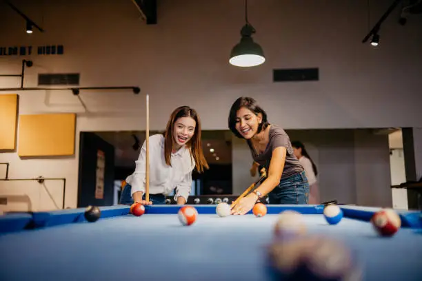 Image of two young woman office workers playing pool in the office. Playing pool with colleague on the break of the workday in the office.