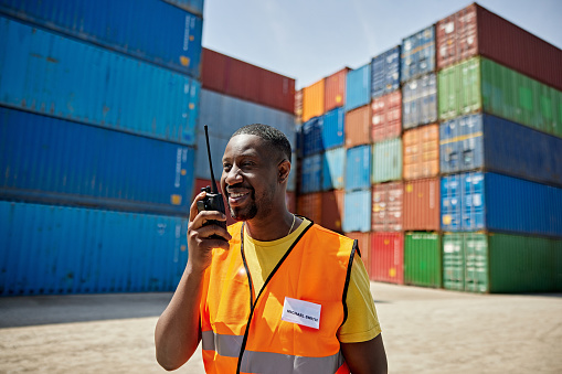 Waist-up view of man wearing reflective vest and communicating with walkie-talkie while standing outdoors at inland container port.