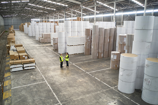 High angle view of male and female coworkers wearing reflective vests and standing together talking in large distribution center.