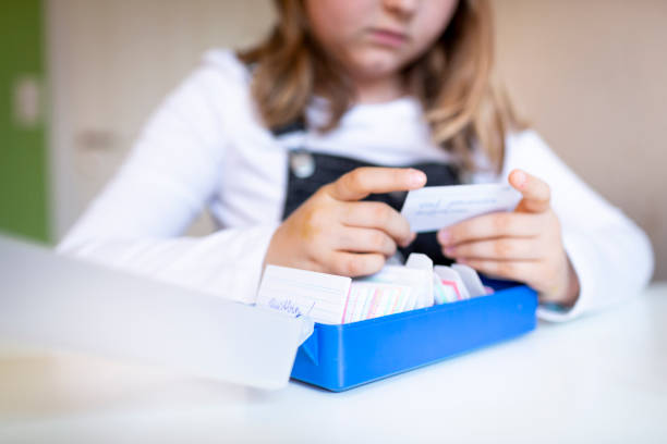 pretty young schoolgirl sitting on her desk in her room at home learning english vocabulary using flashcards - pre teen boy flash imagens e fotografias de stock