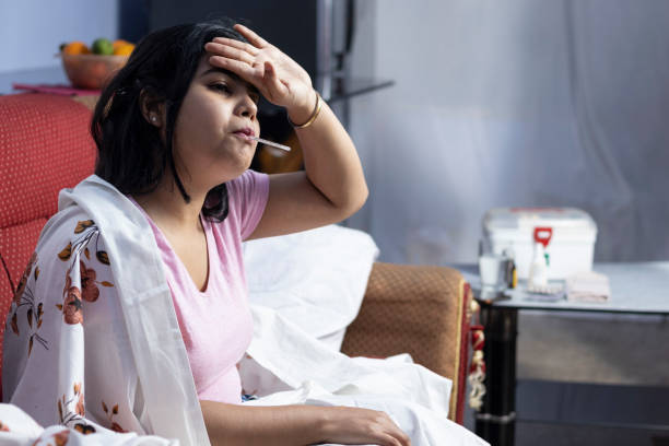 healthcare and medical Selective focus on an Indian woman sitting on sofa with thermometer in mouth during fever fever stock pictures, royalty-free photos & images