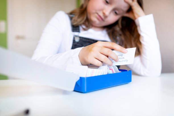 pretty young schoolgirl sitting on her desk in her room at home learning english vocabulary using flashcards - pre teen boy flash imagens e fotografias de stock