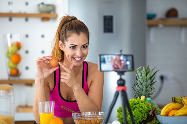 jeune femme dans la vidéo d’enregistrement de cuisine sur l’appareil-photo. - video home video camera shooting video still photos et images de collection