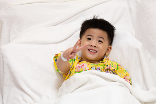 Asian little boy wearing patient outfits lying on the bed in hospital