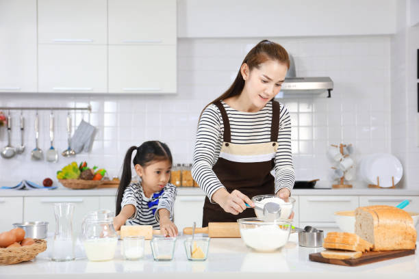 feliz madre asiática enseñando a su hija a hornear pan en la cocina blanca moderna mientras mezcla la receta para amasar harina para hacer masa - bun bread 7 grain bread dough fotografías e imágenes de stock