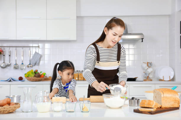 happy asian mother teaching her daughter to bread baking in white modern kitchen while mixing recipe for kneading flour to make dough - bun bread 7 grain bread dough imagens e fotografias de stock