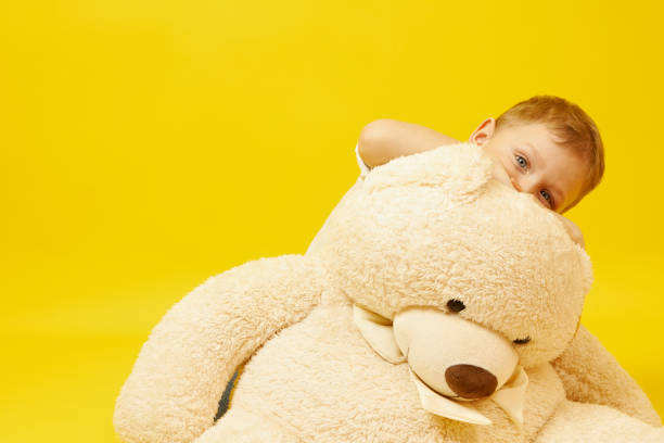 A sad blue-eyed boy with a teddy bear on a yellow background. The emotion of sadness, melancholy, loneliness, sadness.