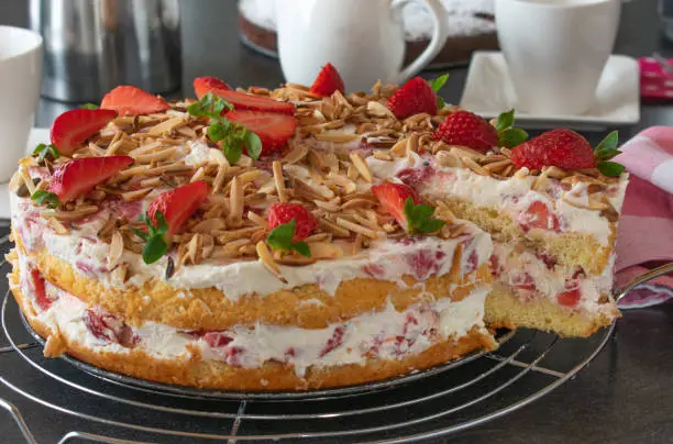 fresh baked strawberry cream cake with chopped and marinated strawberries, whipped cream and homemade biscuit base served on a coffee table. closeup view