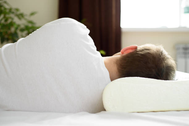 un hombre está descansando sobre una almohada ortopédica. el concepto de cuidar de su salud. sueño saludable, prevención de enfermedades del cuello y la columna vertebral - human vertebra fotos fotografías e imágenes de stock